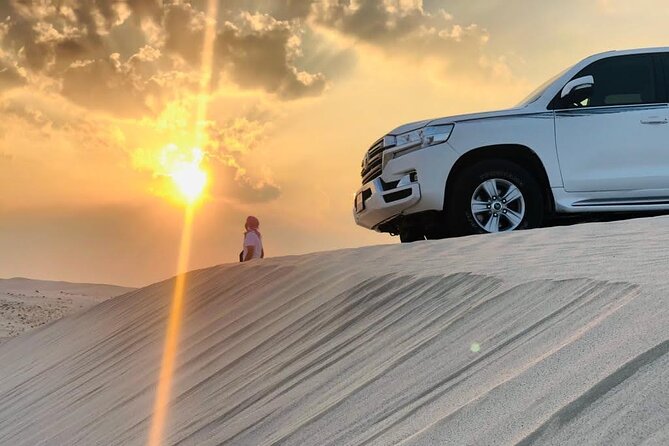 A white safari SUV on a desert dune at sunset